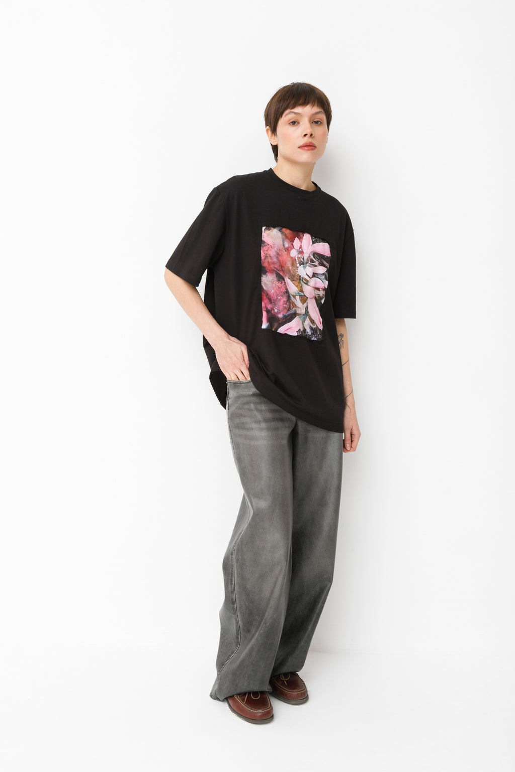 Person wearing a black t-shirt with floral design and gray pants on a white background